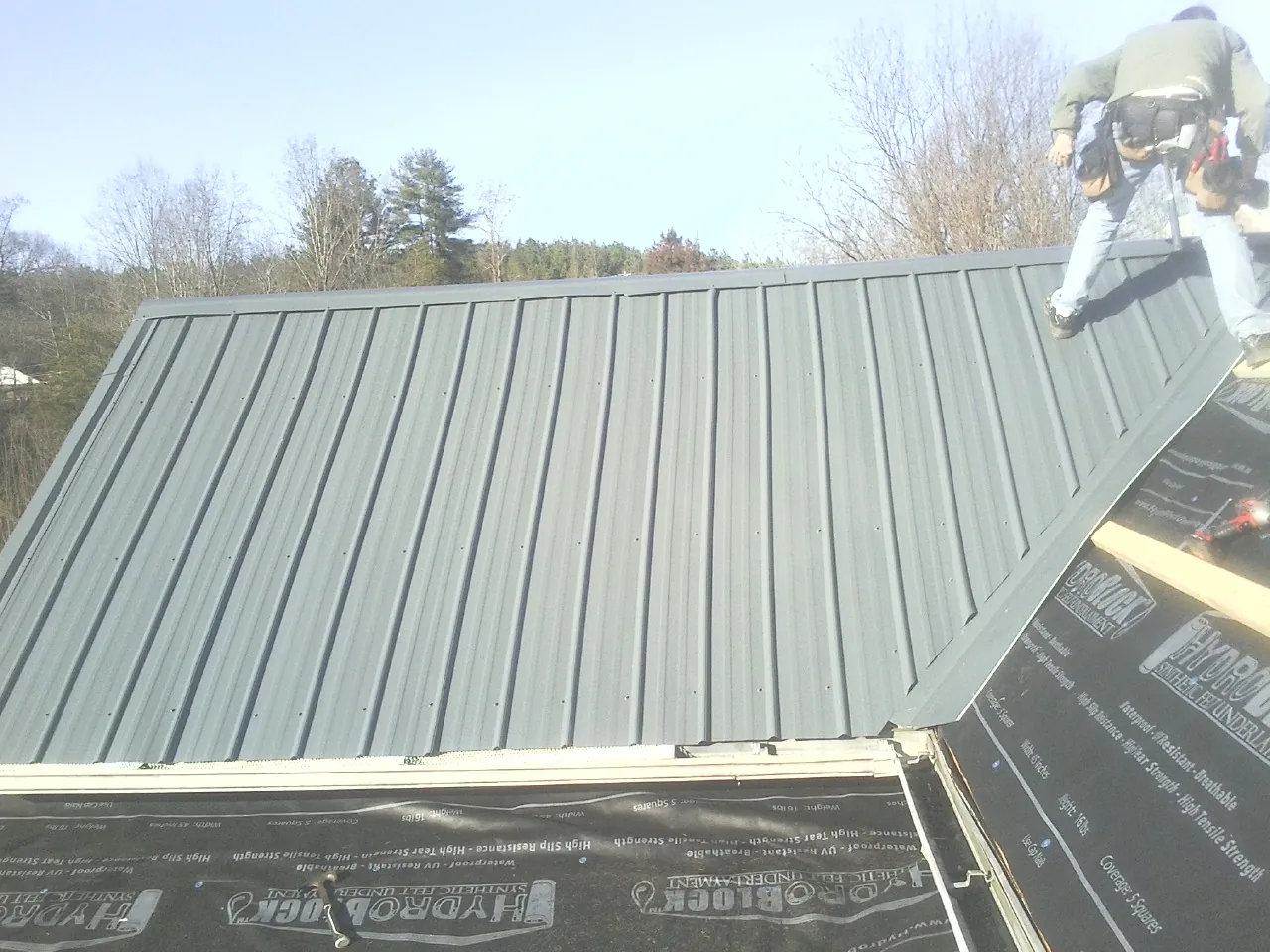 Crew installing dark green standing seam panels over synthetic underlayment in Racine