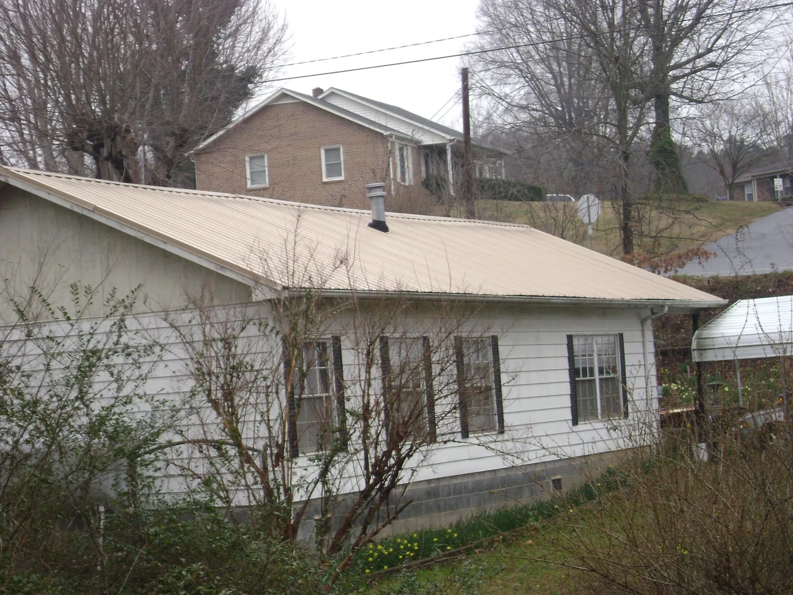 Tan metal roof on a white sided house set into a hillside — Commercial Roofing by Roofing Brothers in Racine